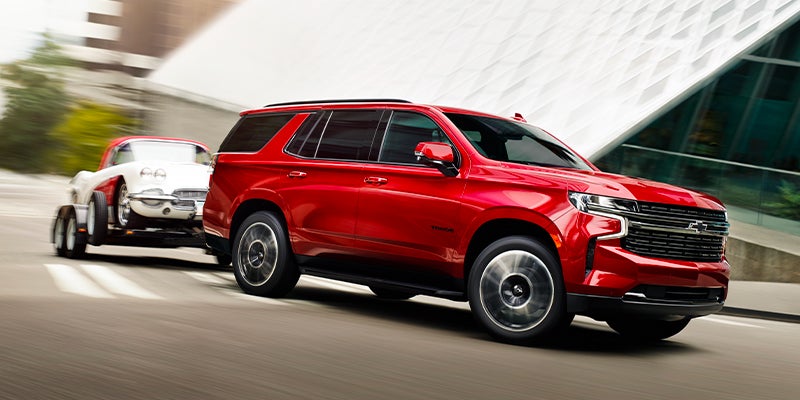 Red 2023 Chevy Tahoe driving on road towing another car on trailer