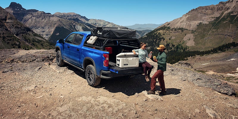 Two people standing at the back of a 2025 Chevy Silverado 1500 with a cooler in the truck bed